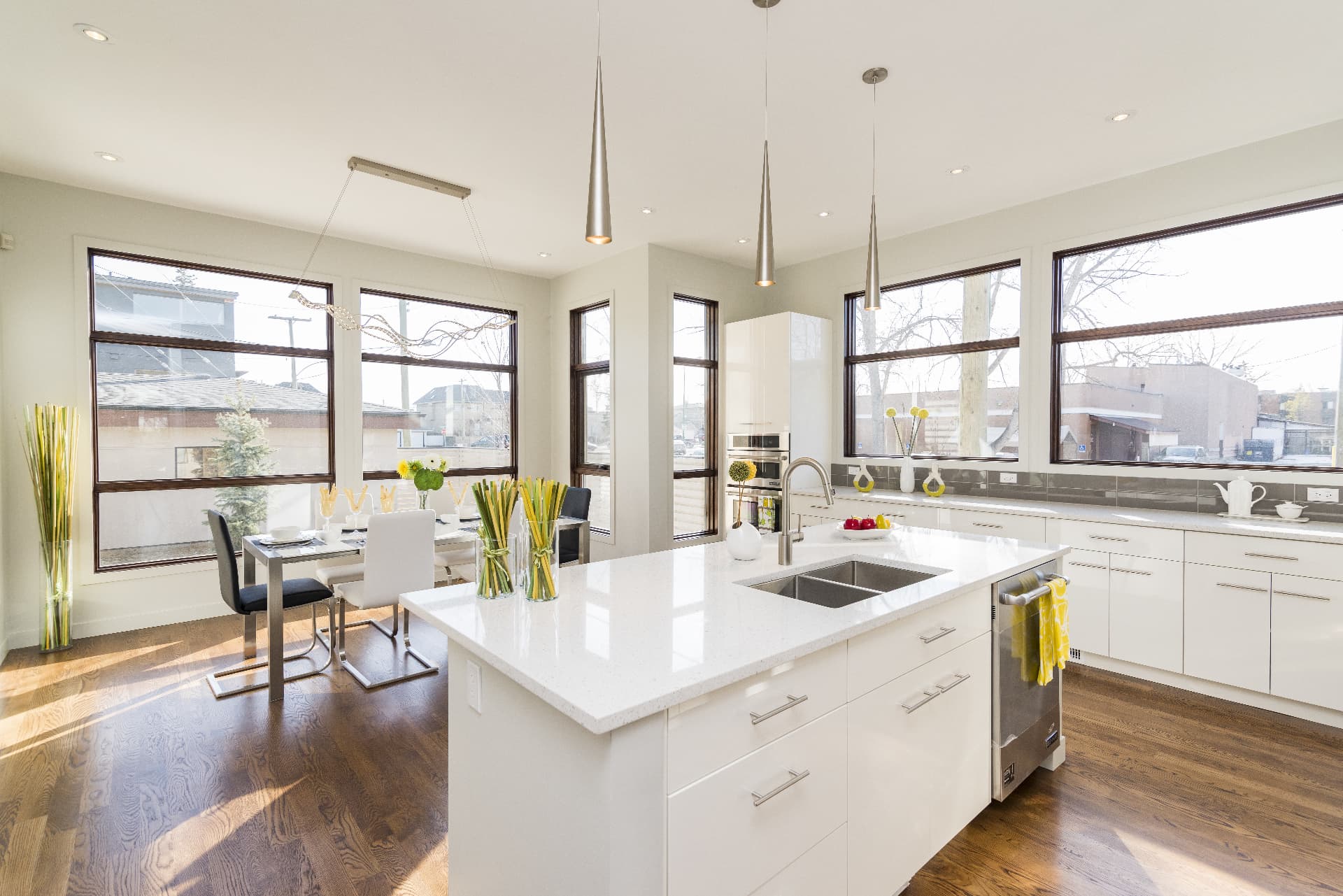 Bright, modern open-concept kitchen with white cabinetry, a large quartz island, and natural light from oversized windows
